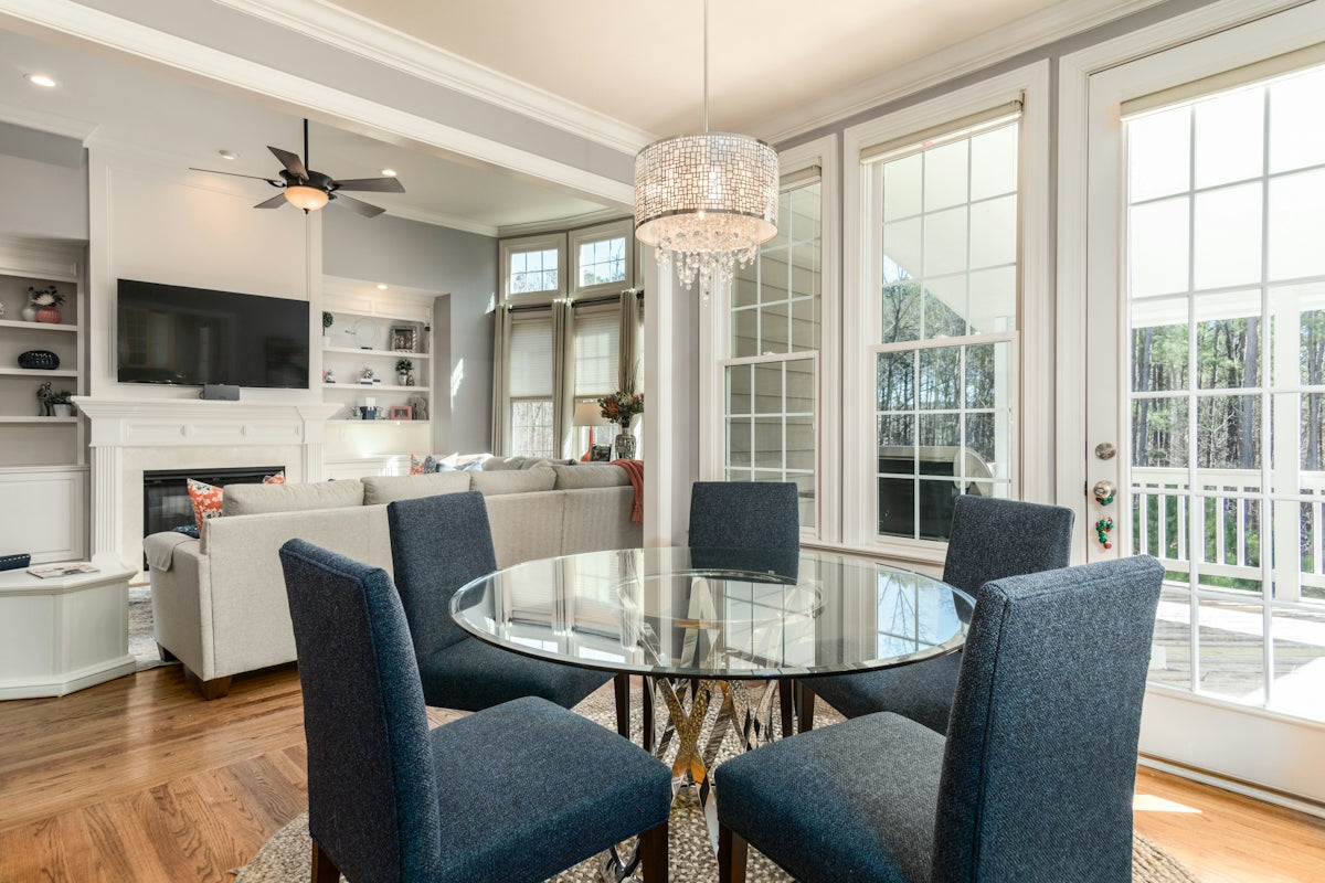 A glass dining table with four blue chairs in a sunlit open living room
