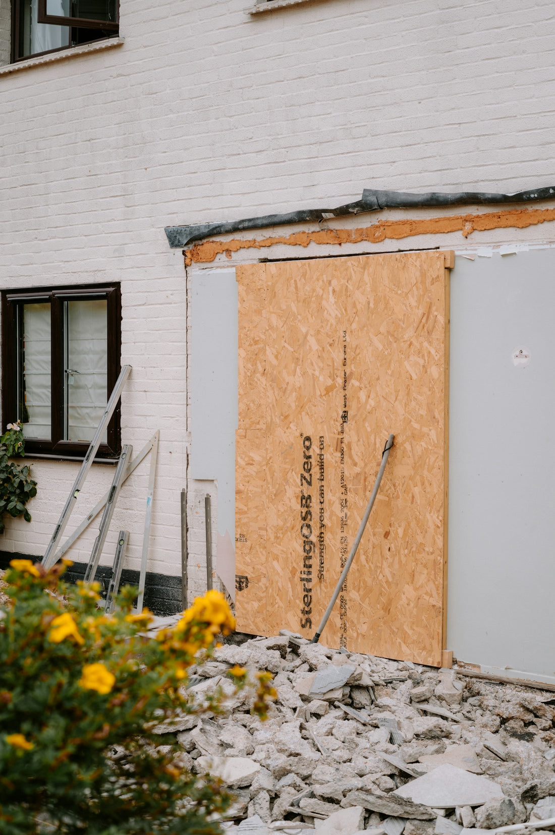 A wooden board covering a doorway on a white brick house under renovation.